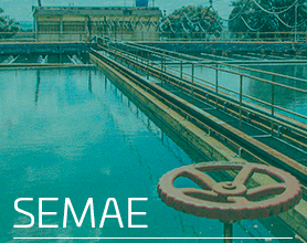 A imagem mostra uma estação de tratamento de água, com um grande tanque de água e diversas estruturas metálicas, incluindo corrimãos e tubulações. No primeiro plano, há uma grande válvula vermelha. Ao fundo, é possível ver um edifício e algumas árvores. O texto "SEMAE" está destacado no canto inferior esquerdo da imagem.